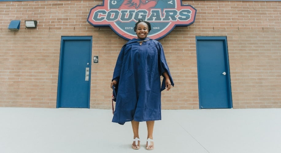 LaToya, a 2019 Lake Trust Foundation Scholarship recipient, stands in a graduation gown in front of a Cleary University Cougars sign