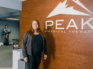 Amy, a Lake Trust business member, stand in front of a sign that says 'Peak Physical Therapy'