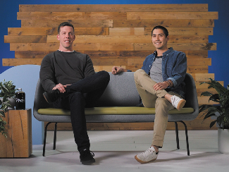 Kevin and Nick, Lake Trust business members who own Tapped Coffee, sit on a couch in front of a wood wall