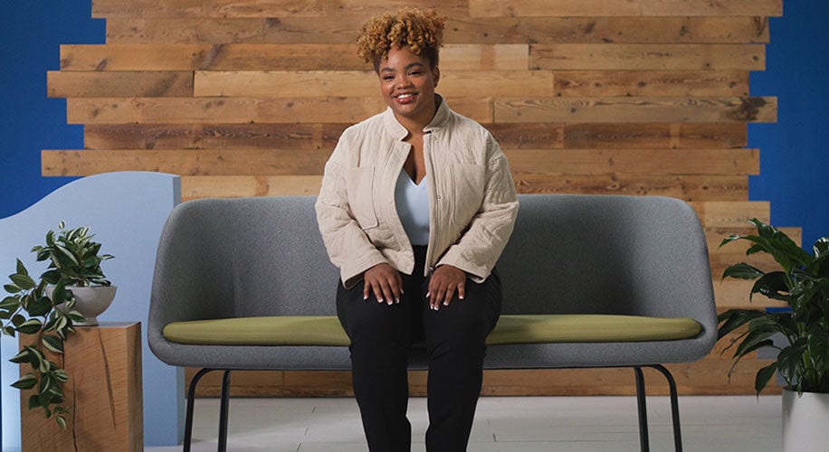 Autumn, the owner of Proxie, sits on a gray and green couch in front of a wood wall