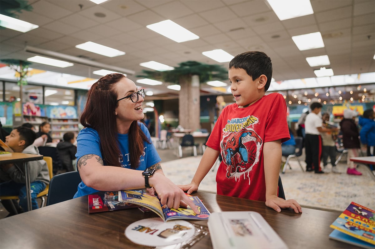 A Lake Trust team member reading a book with a child in a school library.