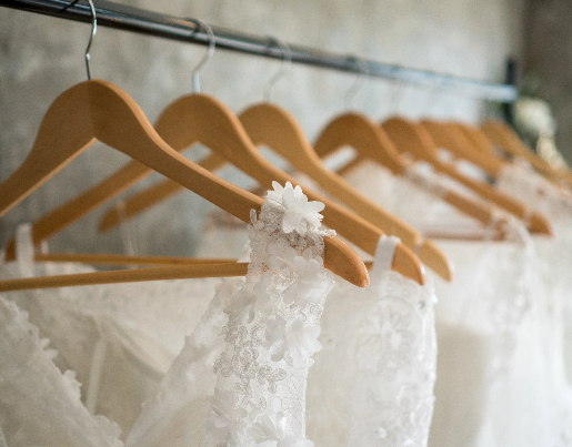 A row of wedding dresses hang on wood hangers