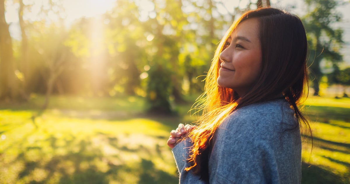 Smiling woman outdoors in a clearing with trees in the background.