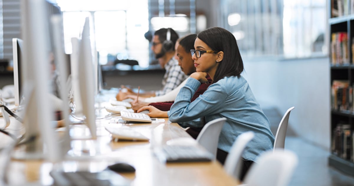 A young woman sits in a row of computers and studies the screen