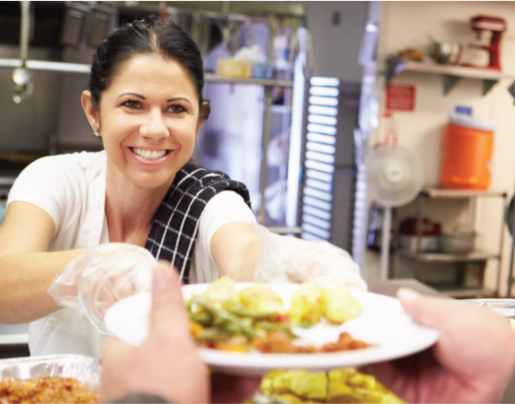 Woman smiling and handing someone a plate of food.