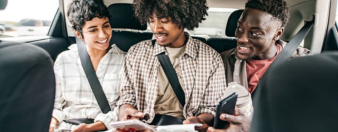 Group of friends sitting in backseat of car sending sending payments through Zelle on their cell phones. 