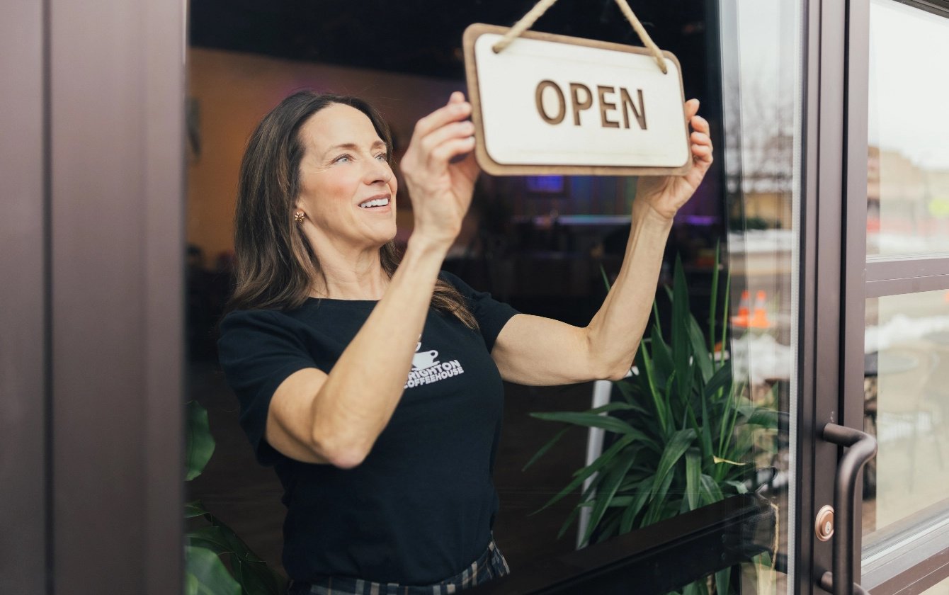 Amy, owner of Brighton Coffeehouse holding "Open" sign.