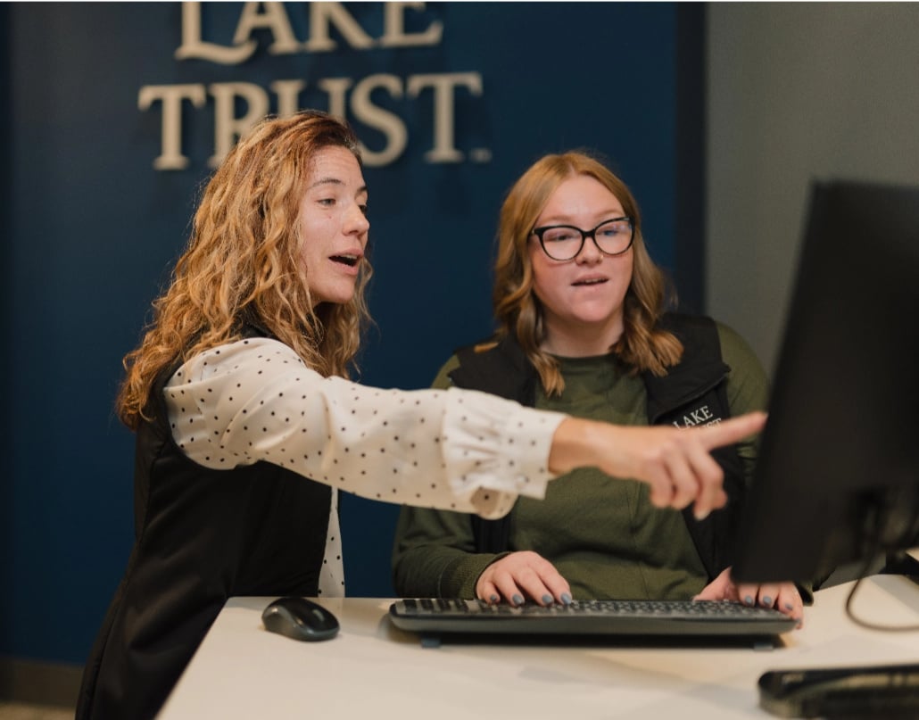 Branch manager helping team member on computer. 