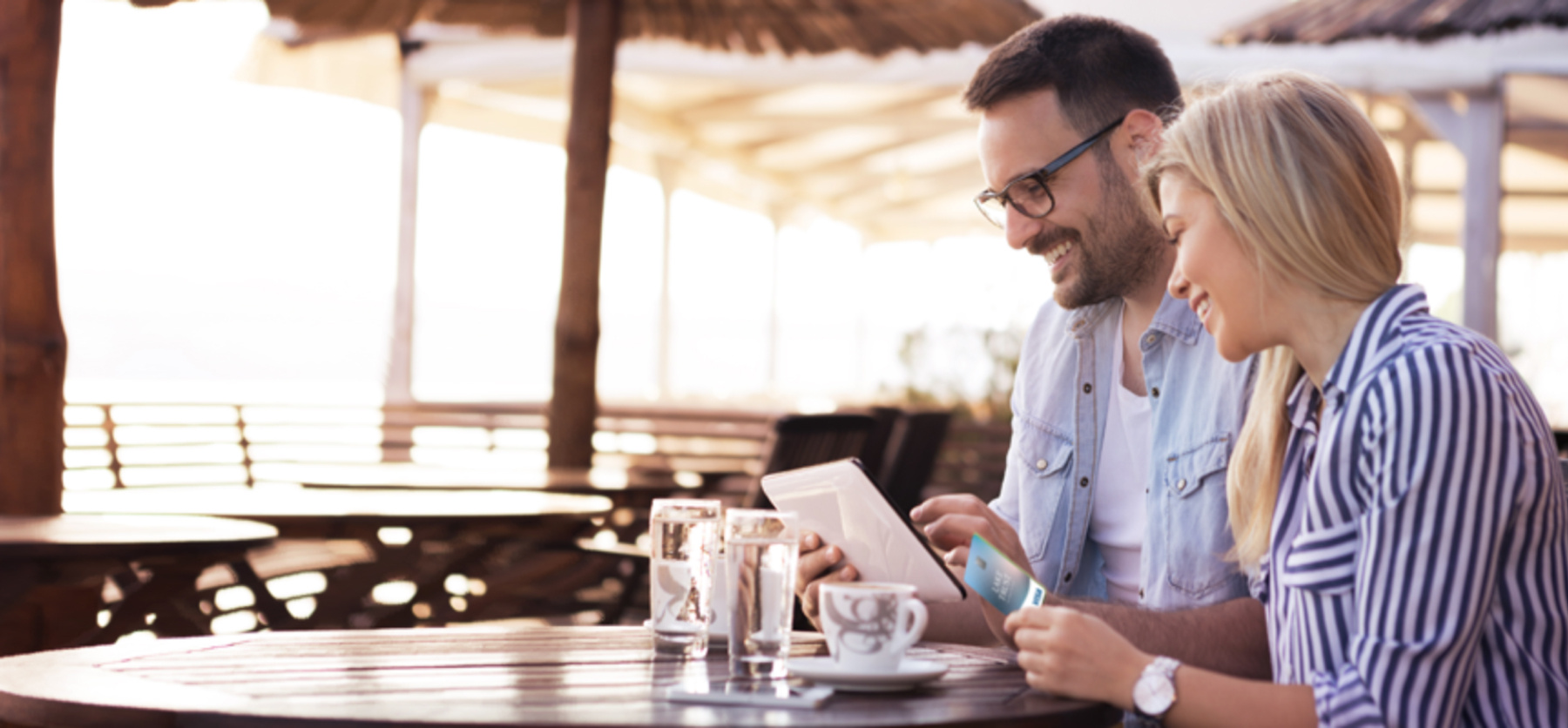 Couple sitting at table looking at iPad, holding Lake Trust credit card. 