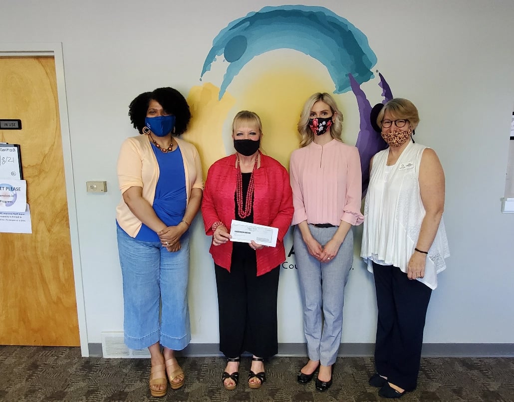 Four women wearing face masks stand in front of a wall with the LACASA logo painted on it