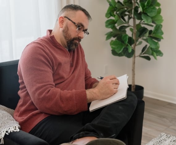 Michael, a Lake Trust member, sits on a black chair and writes in a notebook