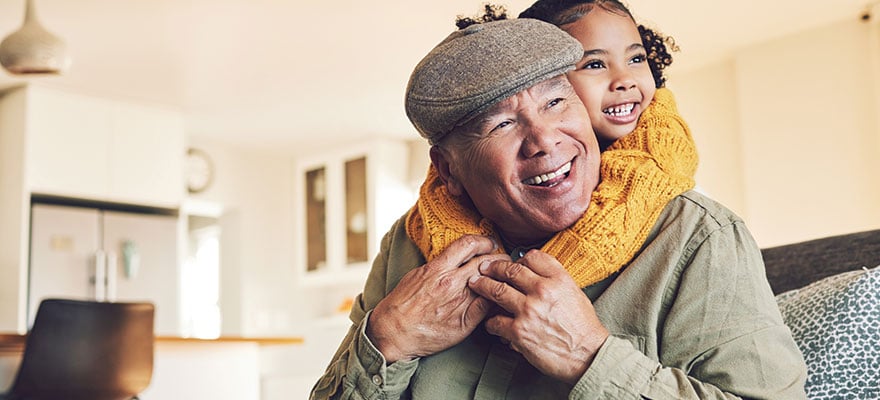 Grandfather and granddaughter smiling together at home, sharing a joyful hug.