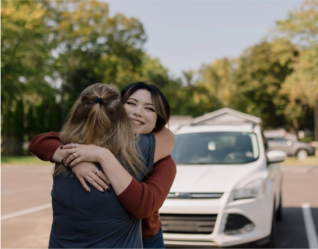 Kadence, a Lake Trust member, hugs a woman in front of a white SUV