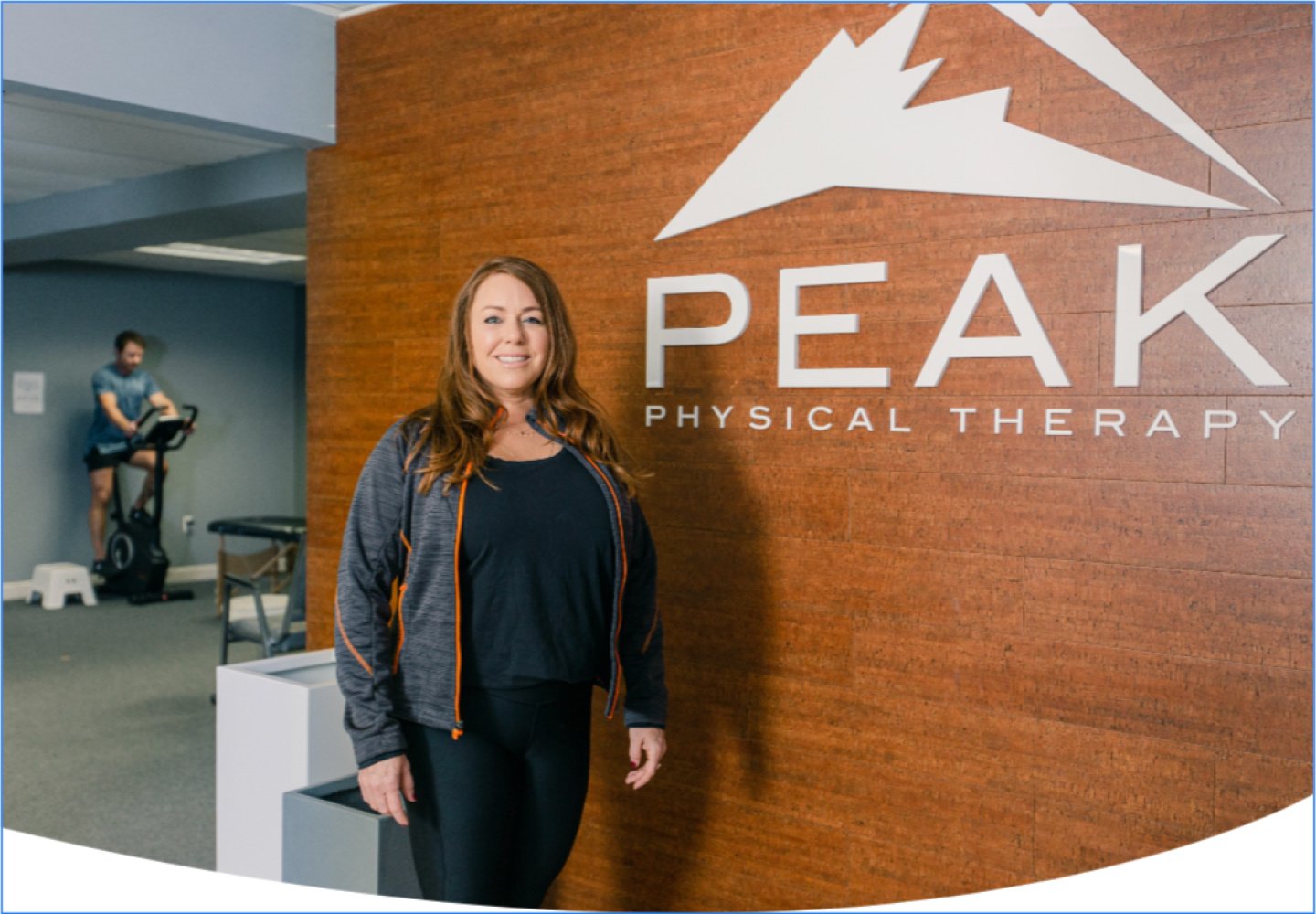 Amy stands in front of a sign that says "Peak Physical Therapy" at her office in Brighton