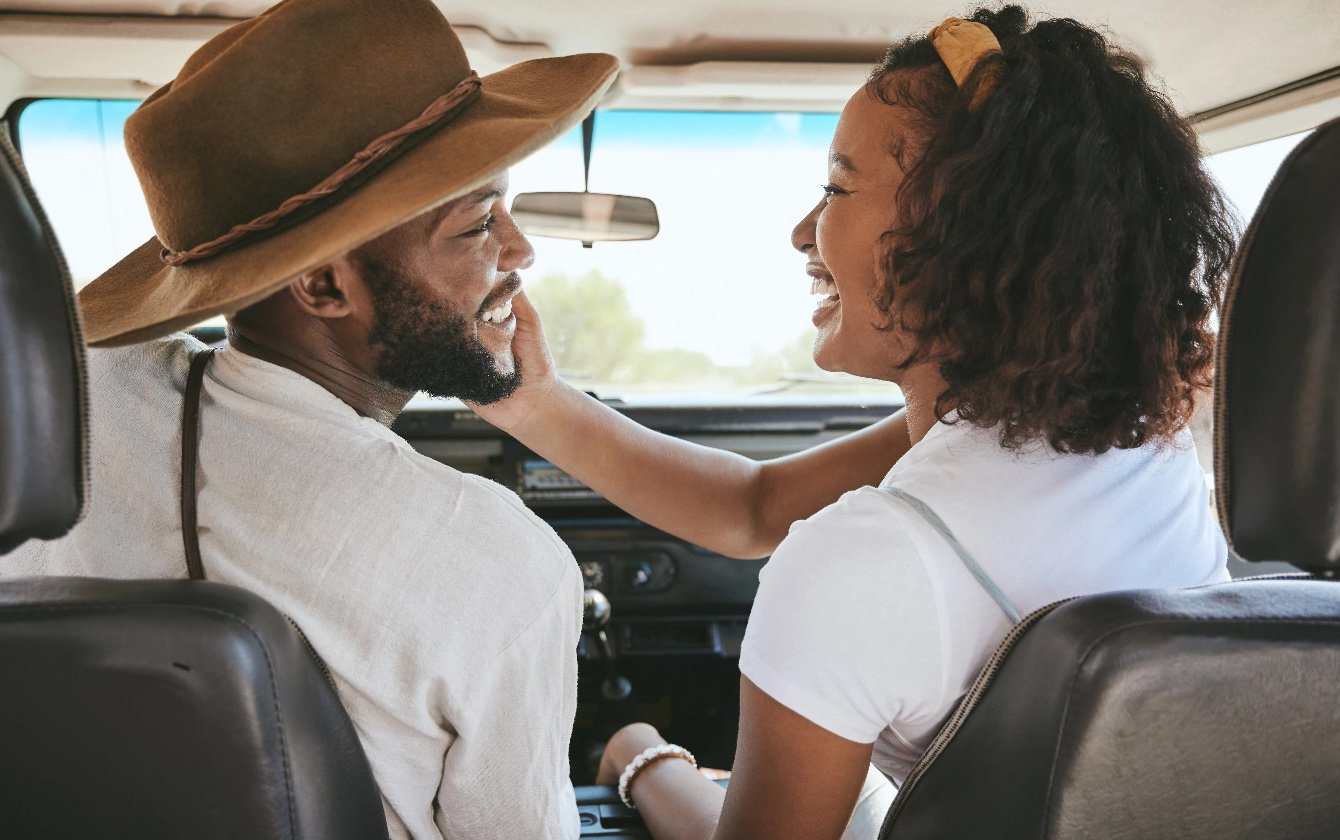 A woman puts her hand on a man's face in the front seat of a car