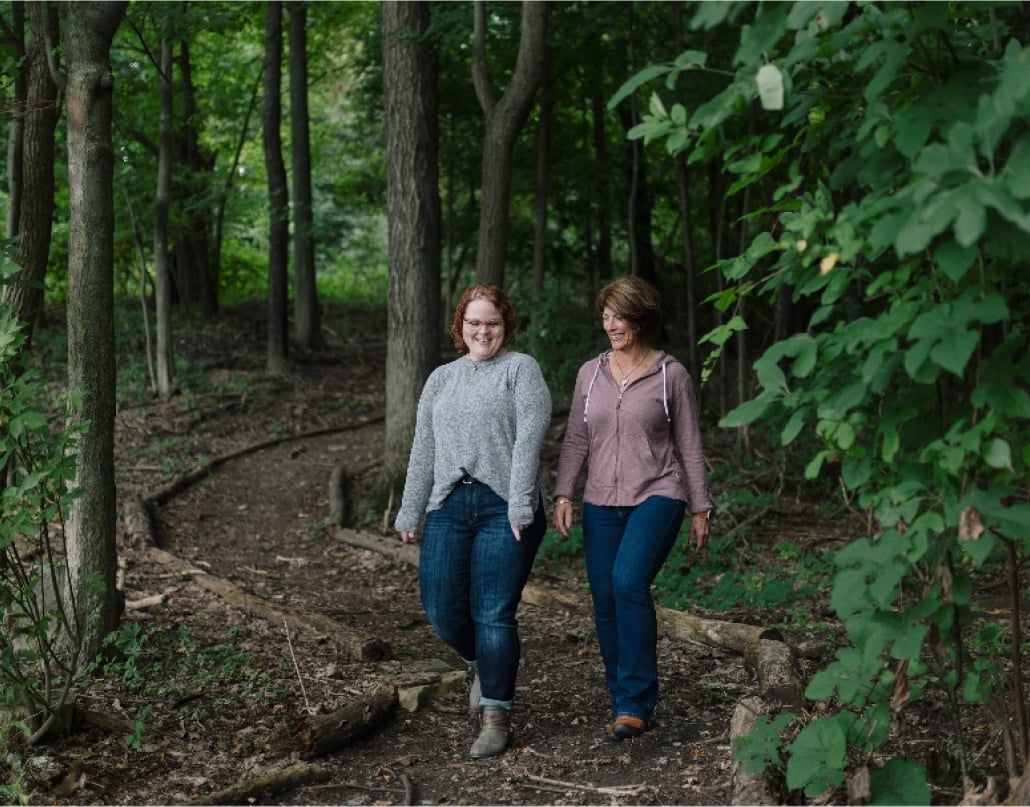 Two women walk on a path through the woods