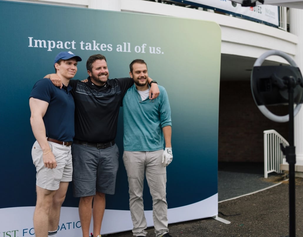 Three men stand in front of a backdrop that says "Impact takes all of us"