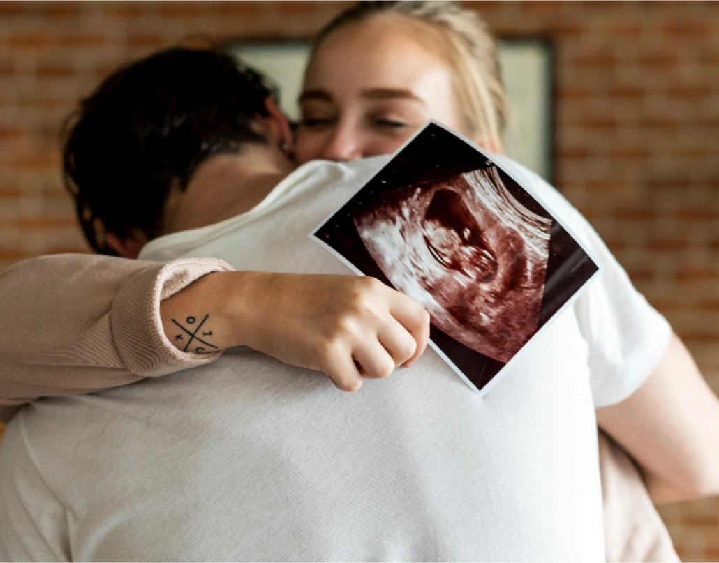 A woman holding an ultrasound picture hugs a man