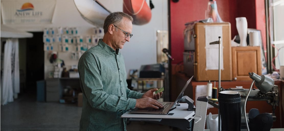 Business member holding Lake Trust credit card and typing on laptop.